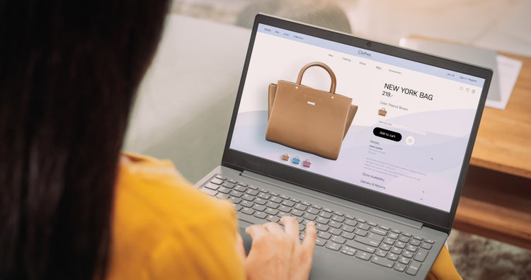 Over-the-shoulder shot of a woman using her laptop to view product photos and videos of a bag on an ecommerce platform.