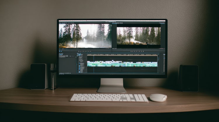 An iMac on a table showing the Adobe Premiere interface.