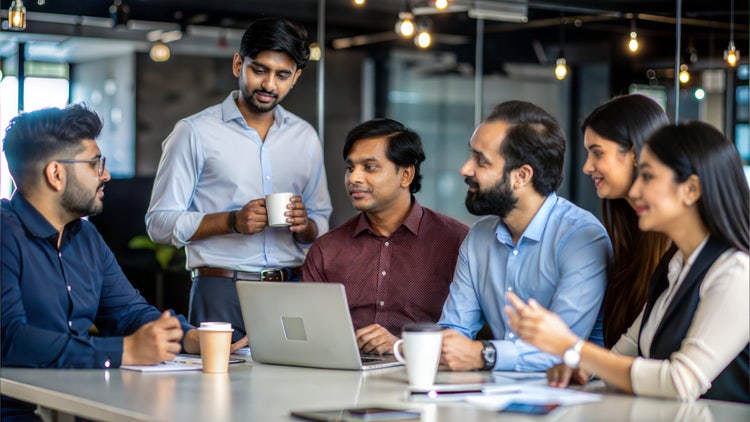 Indian creative professionals discuss ai solutions in a modern office with laptops and coffee