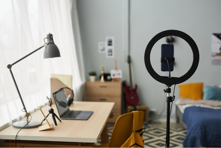 Modern bedroom workspace with ring light and smartphone on tripod, ideal for recording UGC ads and social media videos.