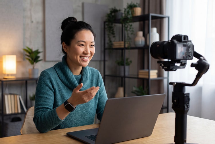 A smiling woman filming a video resume with a laptop and professional camera in her home office.