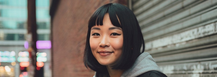 An AI-generated image of a cool-looking young women with a bright smile standing on a city street against a brick wall and sheet-metal garage door.