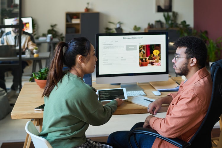 Two people discussing ai image generator on computer screen in modern office with plants and tablets.
