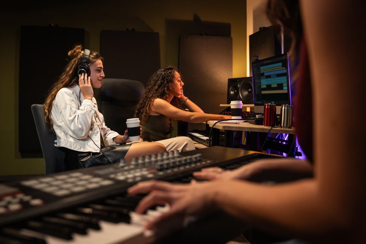 Music producers using AI sound generator software on computer in recording studio with keyboard and headphones.