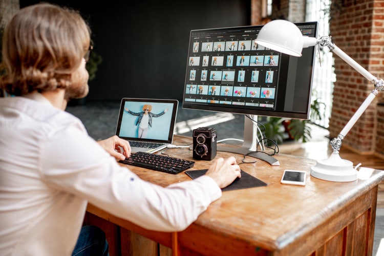 Designer using image expander software on dual screens to edit portraits at a desk in a modern studio.