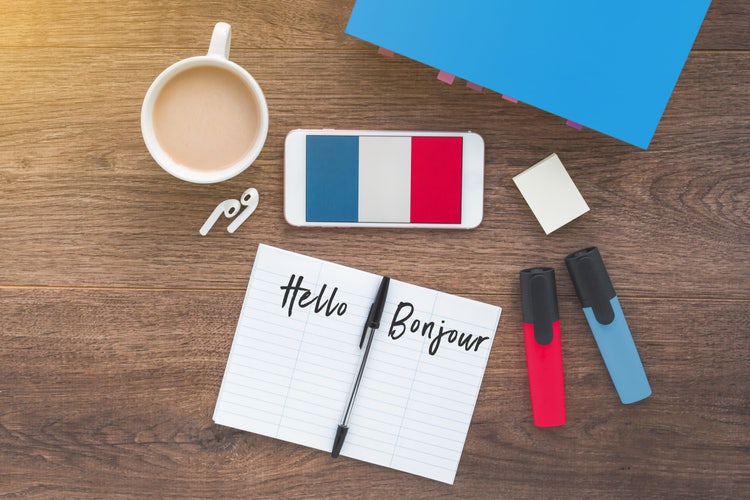 A table with books, including one labelled “Hello” and “Bonjour”, a phone showing the French flag, earphones, a highlighter and a cup of tea.
