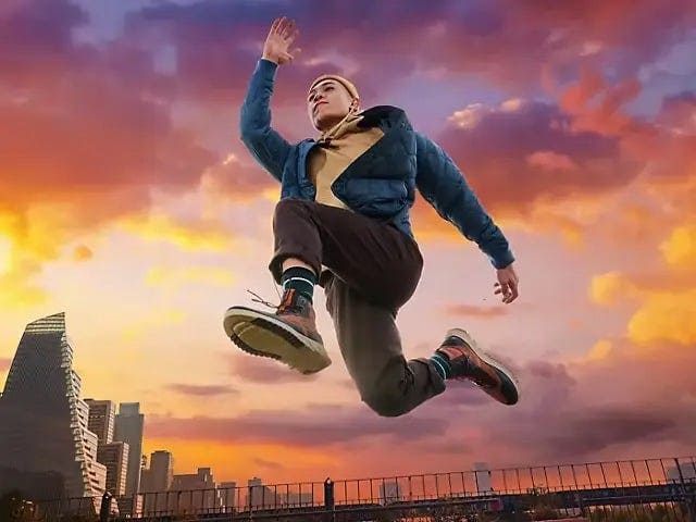 AI-enhanced photo of man mid-leap against vibrant sunset sky and city skyline, showcasing Adobe Photoshop sky replacement feature