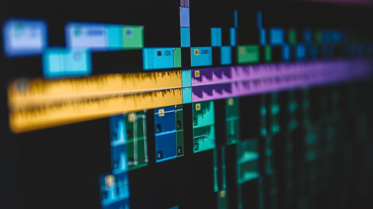 Close-up of a video editing timeline in Adobe Premiere Pro showing multiple layered audio and video tracks with colour-coded clips and effects applied.