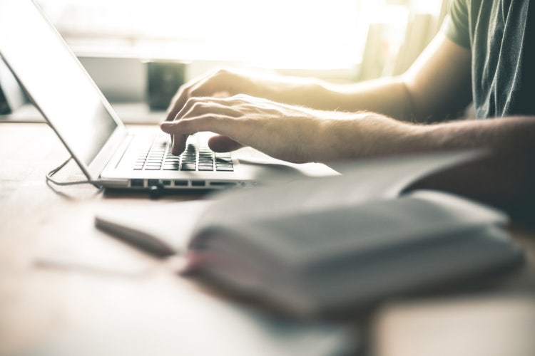 Mani di un uomo che digitano al computer.