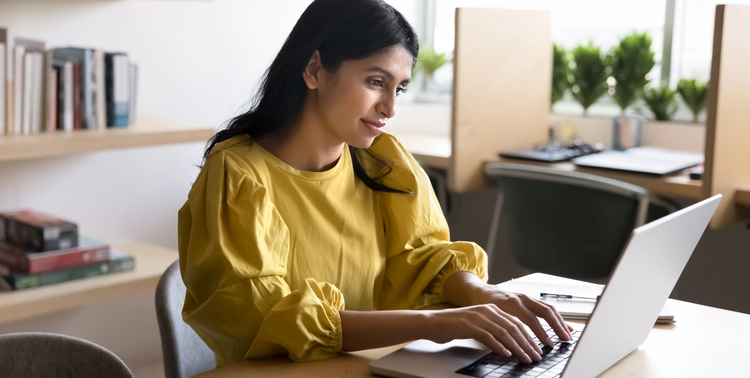 Donna con maglia gialla digita su un computer seduta a una scrivania.