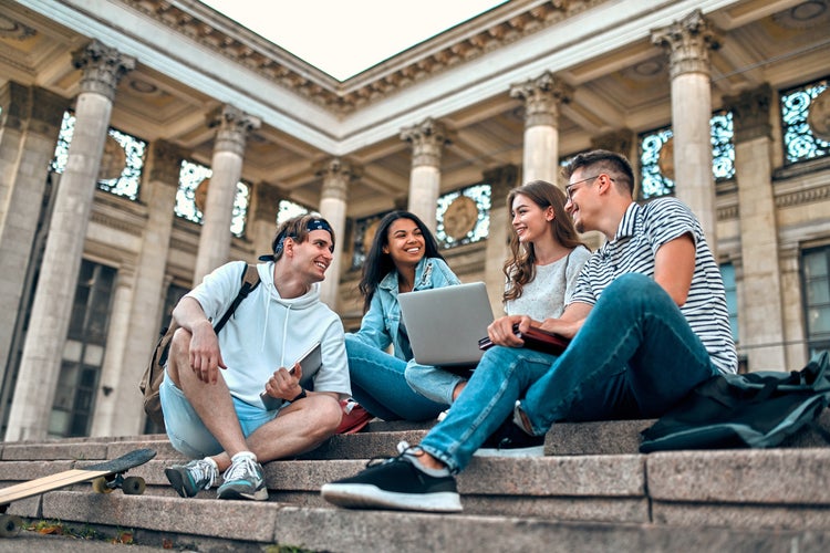 Gruppo di studenti con un computer portatile seduti sulle scale di un campus universitario