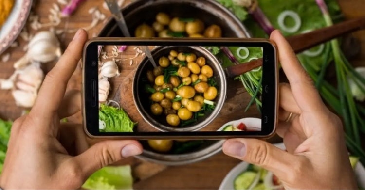 Persona che fotografa un piatto di cucina con smartphone per ricettario digitale