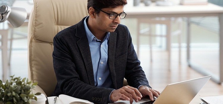Un uomo seduto alla scrivania di un ufficio intento a lavorare con un laptop.