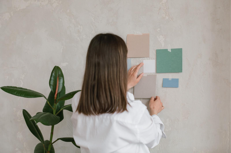 Una donna che appende campioni di colore a una parete, cercando ispirazione per una moodboard di interior design.
