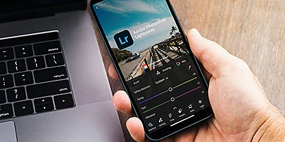 Una persona che tiene in mano il telefono e utilizza l’app di Adobe {{lightroom}}