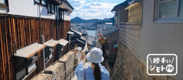 海へ続く坂道で、街並みを撮影する旅行者