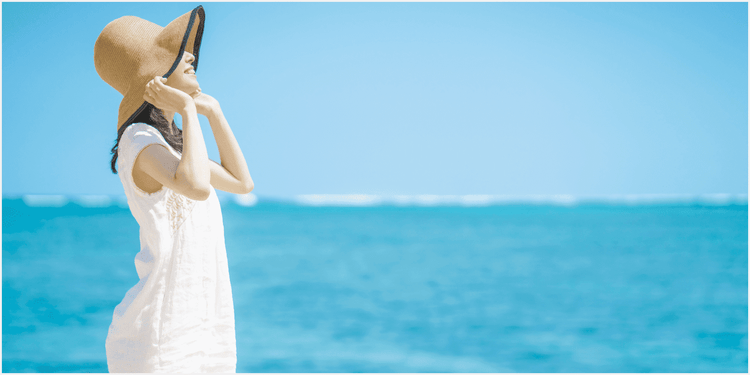 青く澄んだ海と空を背景にした、帽子を押さえた女性