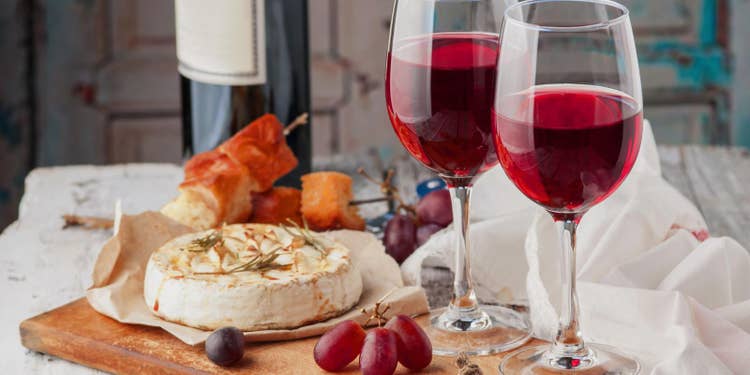 白いテーブルに茶色のカッティングボード、赤ワインとチーズ