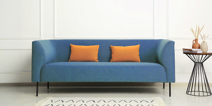 白い壁を背景とした、青いソファとオレンジ色のクッション