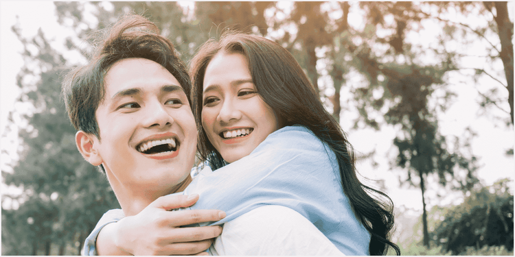 林の中で、笑顔の男性に後ろから抱き着く笑顔の女性