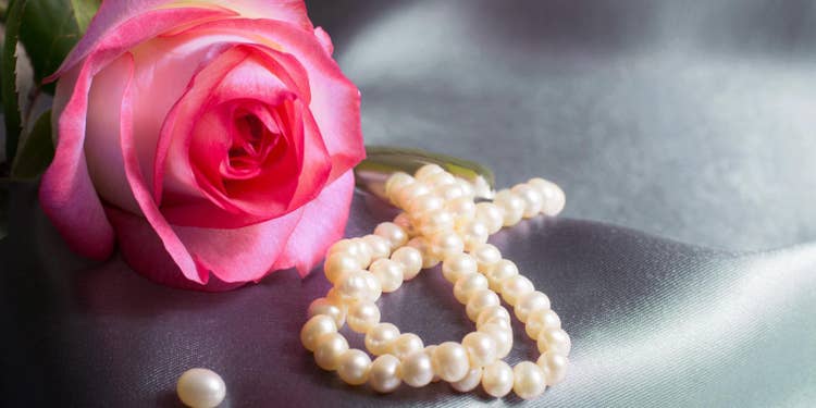 ブルーグレーの布を背景とした、ピンクのバラと白いパールのアクセサリー