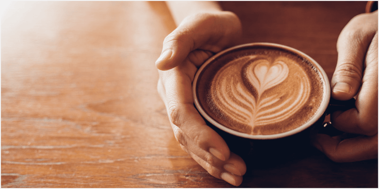 ラテアートされたコーヒーカップと、カップに添えた手