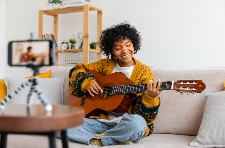 Girl with guitar A young girl sits on a sofa with a guitar in her arms. A phone on a tripod records her.