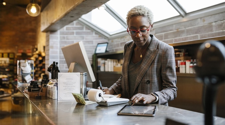 Woman in business attire and red glasses reviewing a contract on a tablet and doing accounting tasks