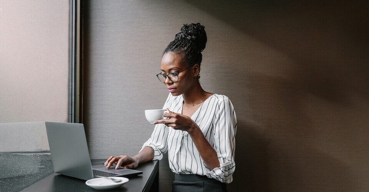 A person holding a cup of coffee in one hand and using their laptop to review a document with a digital certification