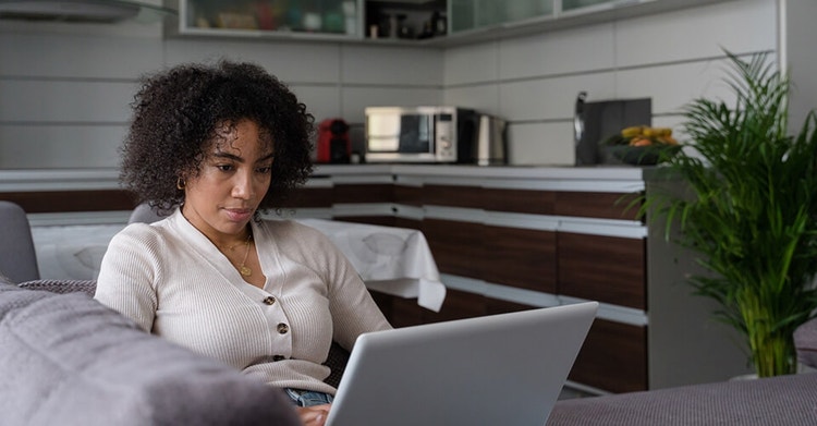 A woman reclining on a couch while providing an s-signature on an electronic document on their laptop