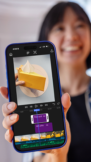 https://main--cc--adobecom.aem.page/cc-shared/fragments/products/premiere/app/unlimited-tracks#unlimited-tracks | 편집 타임라인에서 노란 종이 케이크 비디오가 재생되는 앱 UI가 표시된 휴대폰을 들고 있는 여성의 비디오 스틸. | :play:
