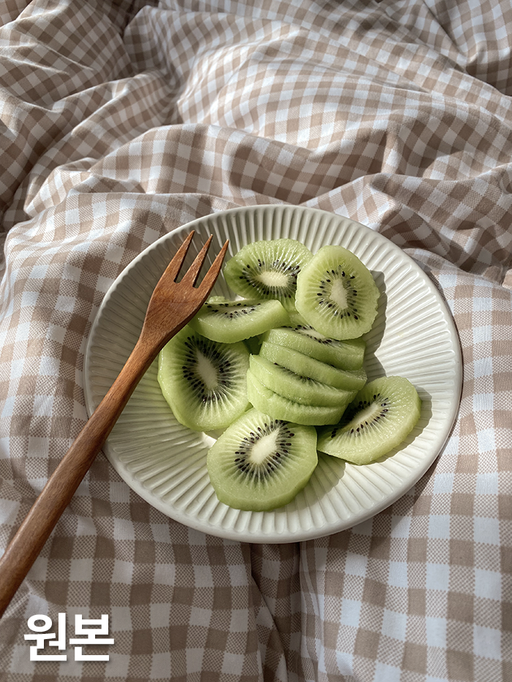 체크무늬 이불 위에 올려진 키위 접시와 포크가 얹혀 있는 원본 이미지