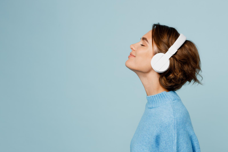 woman in blue shirt with white headphones over her ears and eyes closed over a blue background