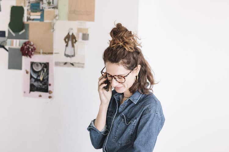 Brunette woman in a denim shirt and turtleshell glasses talking on her phone