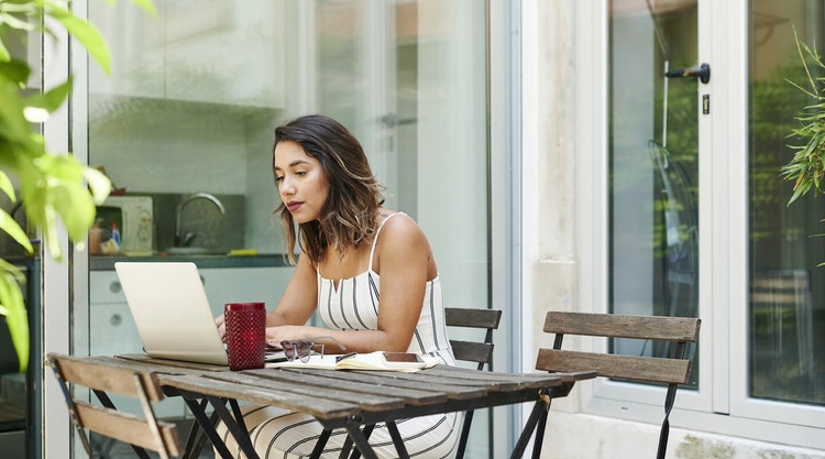 Woman sitting outside in a white jumpsuit while reviewing a landscape contract on her laptop
