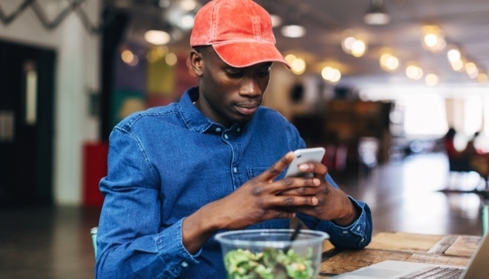 Hombre con gorra roja usando su celular en la hora del almuerzo