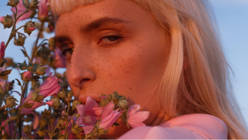 https://video.tv.adobe.com/v/3471140?autoplay=true&end=replay&hasaudio=false&mute=false&chrome=false | An AI-generated woman with blond hair holds flowers near her face showcasing how the AI video generator captures fine details.