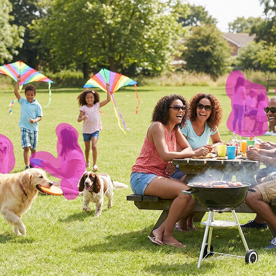 A group of adults gather at a picnic table while children play with kites. Unwanted people in the background are highlighted for removal.