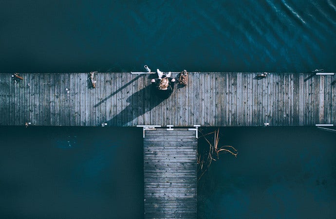 Aerial shot ng isang babae sa pier na nagpapakita na siya ay nag-iisa at napapaligiran ng tubig.