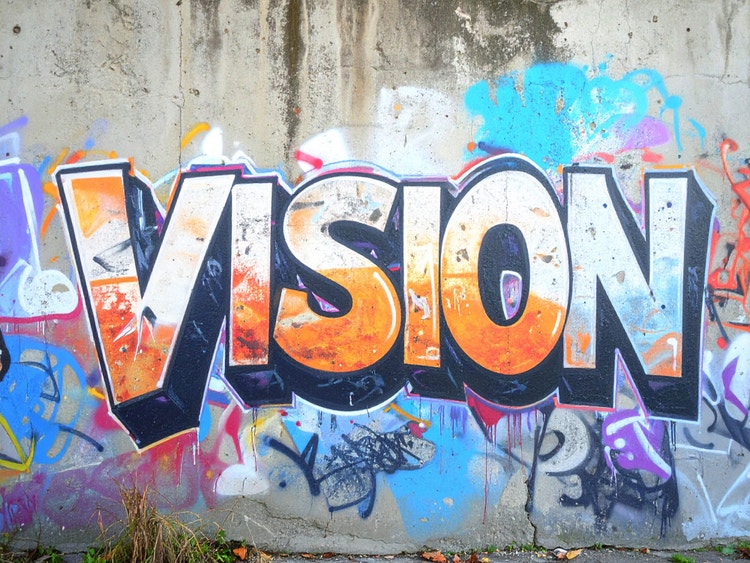Colorful graffiti covers a brick wall, displaying various artistic designs and prominently featuring the word "Vision."