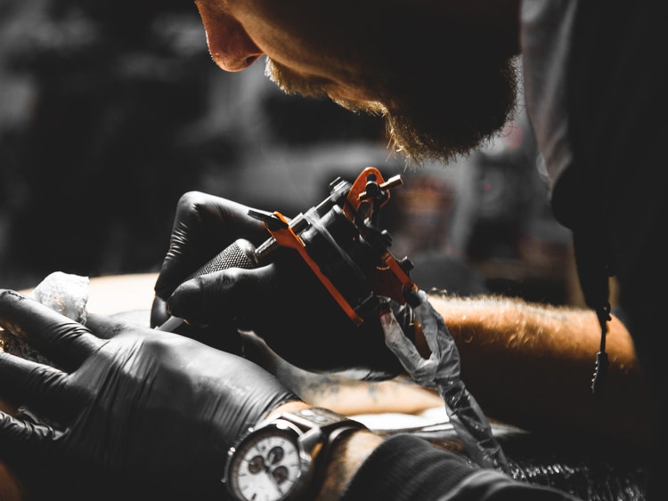 Close-up of a tattoo artist wearing gloves while using a tattoo machine to ink a design on a client.