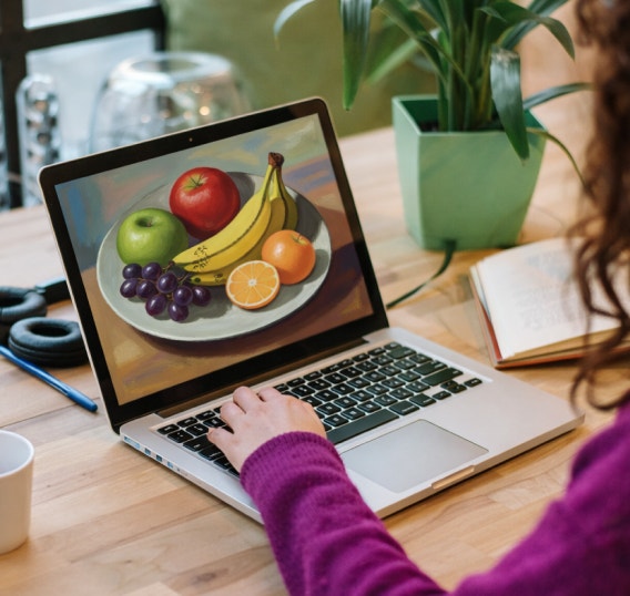 A woman at a computer creating a still life image of fruit. UI in the lower left corner shows the same image of fruit.