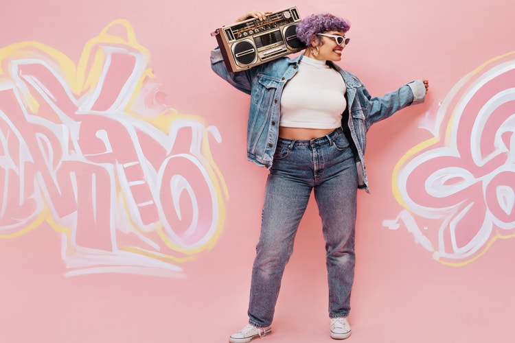 A smiling woman with purple hair and glasses enjoys music from a boombox, set against a colorful pink graffiti wall.