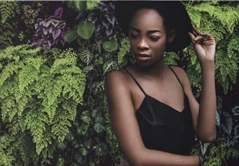 A photo of a person. The background has been replaced with a leafy green background.