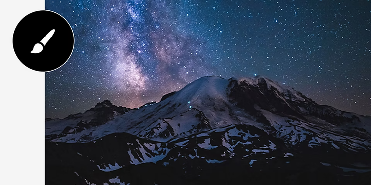 A snowy mountain range at night is topped by stars among a purple-and-blue galaxy with brush tool icon overlaid