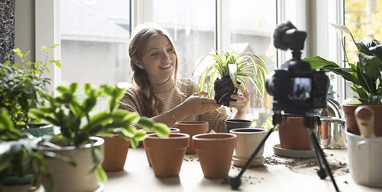 Person using a DSLR camera on a tripod to record a video of themselves planting plants