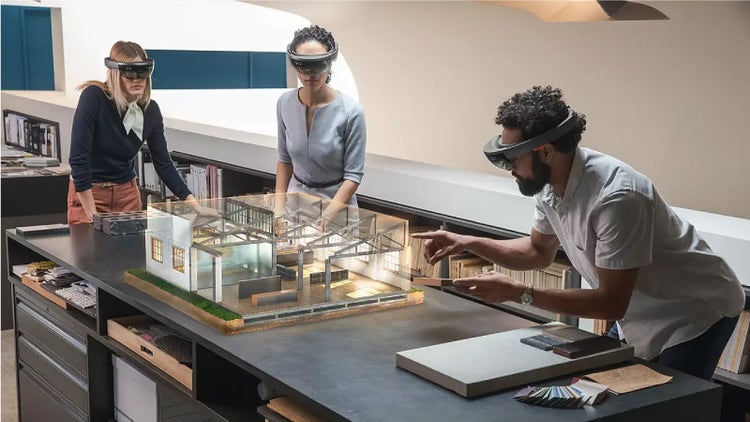 people using mixed reality goggles to manipulate a virtual 3D rendering of a house