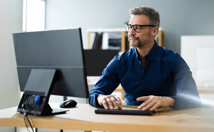 Um homem sentado a uma secretária numa sala cheia de luz, a utilizar um computador de secretária para rodar um PDF no Windows 10.