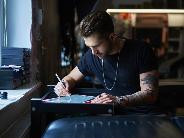 Pessoa desenhando a arte de uma tatuagem em um tablet digital em um espaço de trabalho de estúdio.