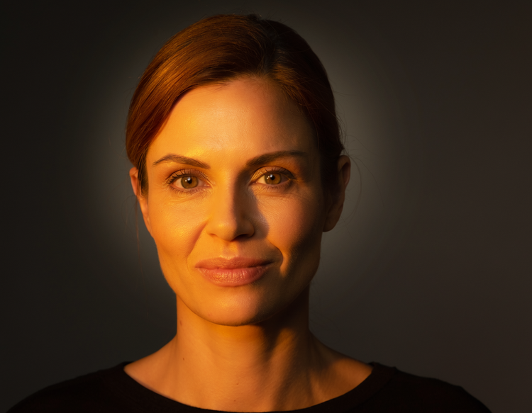 Un portret fotorealist, creat cu Adobe Firefly, al unei femei fictive în vârstă de aproximativ 30 de ani, cu o expresie încrezătoare, cu iluminare caldă de studio.